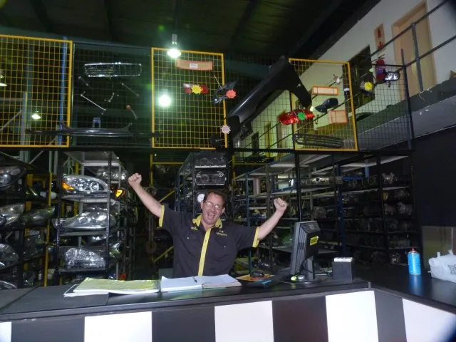 A SparesBoyz team member at the warehouse counter with racking of headlamps behind